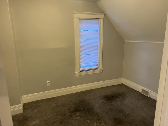 bonus room featuring lofted ceiling, visible vents, dark carpet, and baseboards