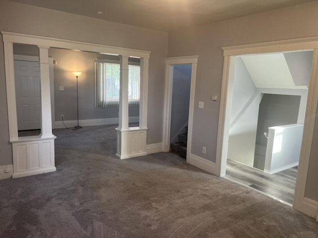 carpeted empty room featuring stairs, decorative columns, and baseboards