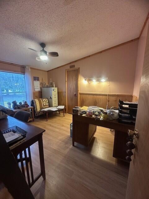 office featuring a ceiling fan, wainscoting, wood finished floors, crown molding, and a textured ceiling