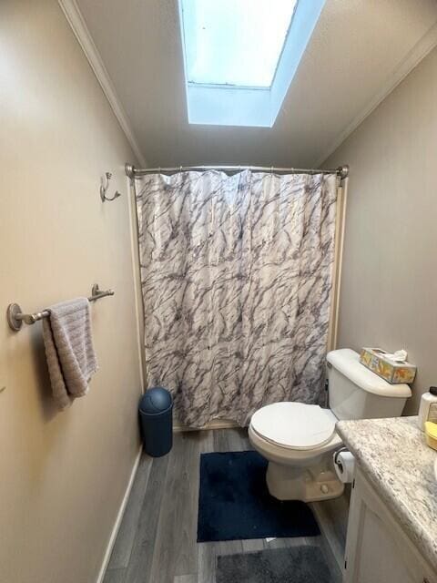 bathroom with toilet, wood finished floors, vanity, ornamental molding, and lofted ceiling with skylight