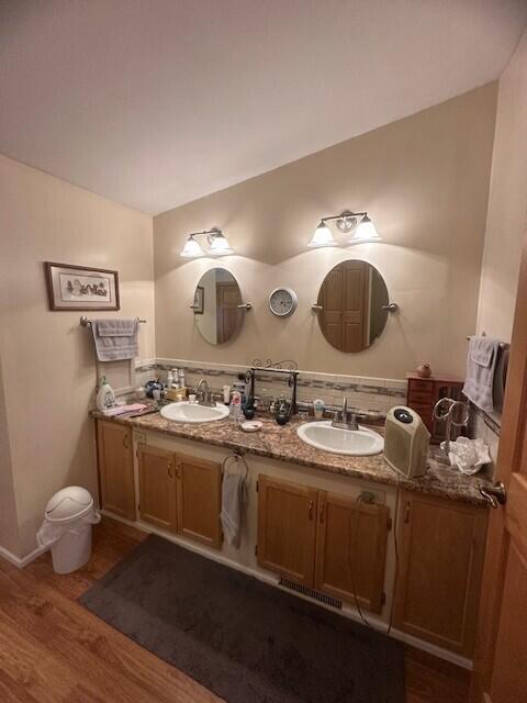 full bath with double vanity, baseboards, a sink, and wood finished floors