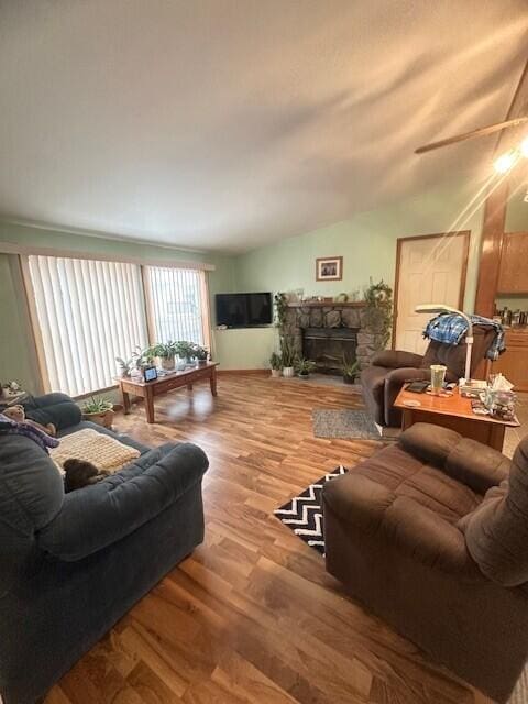 living area with vaulted ceiling, a stone fireplace, and wood finished floors