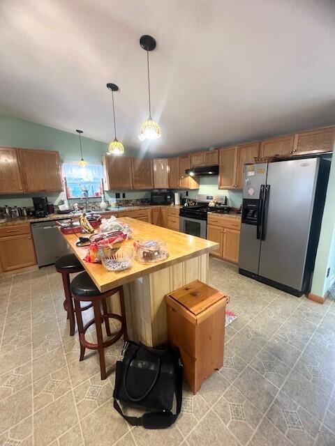 kitchen with decorative light fixtures, a breakfast bar area, lofted ceiling, appliances with stainless steel finishes, and under cabinet range hood