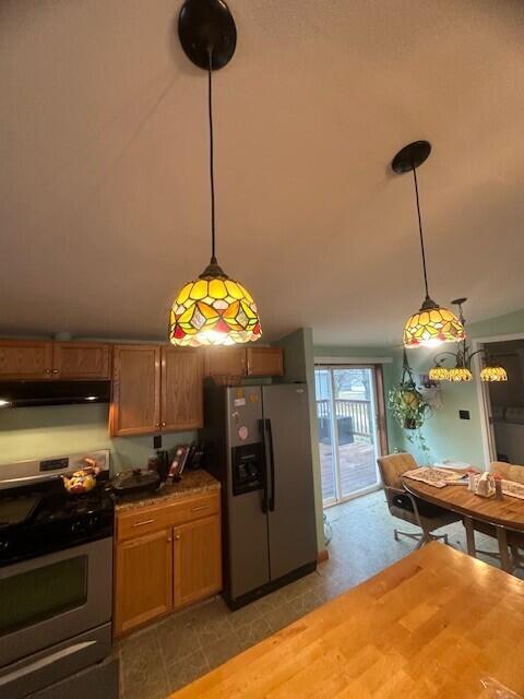 kitchen featuring brown cabinetry, lofted ceiling, decorative light fixtures, stainless steel appliances, and under cabinet range hood