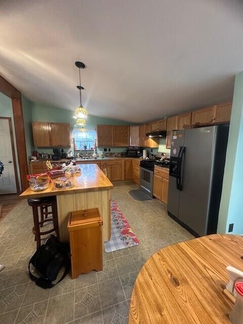 kitchen with stainless steel range with gas cooktop, light countertops, vaulted ceiling, refrigerator with ice dispenser, and under cabinet range hood