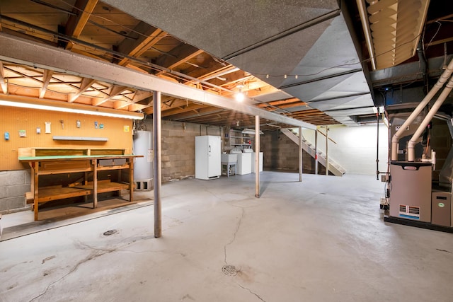 unfinished basement with gas water heater, a sink, freestanding refrigerator, washer / clothes dryer, and a workshop area