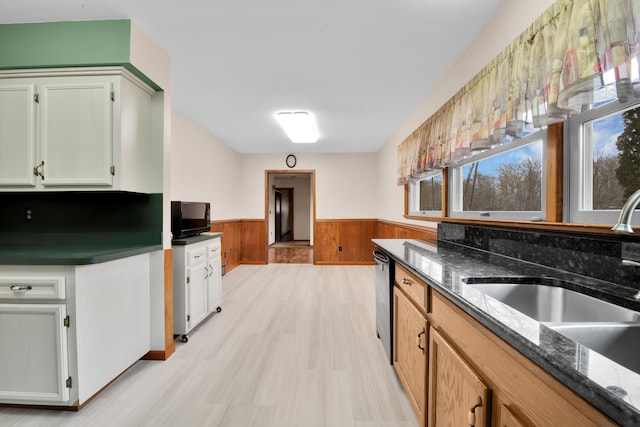 kitchen with a wainscoted wall, dark stone countertops, a sink, and dishwasher