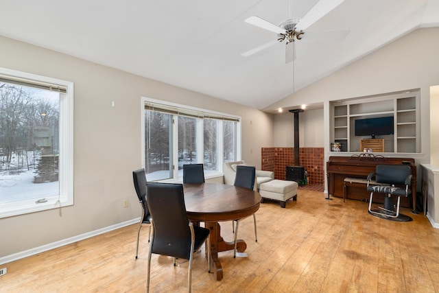 dining room featuring a wood stove, plenty of natural light, vaulted ceiling, and light wood-style flooring