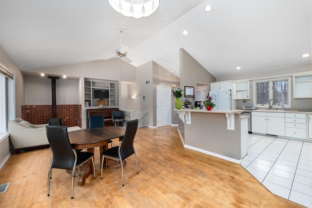 dining space with visible vents, ceiling fan, a wood stove, vaulted ceiling, and light wood-type flooring