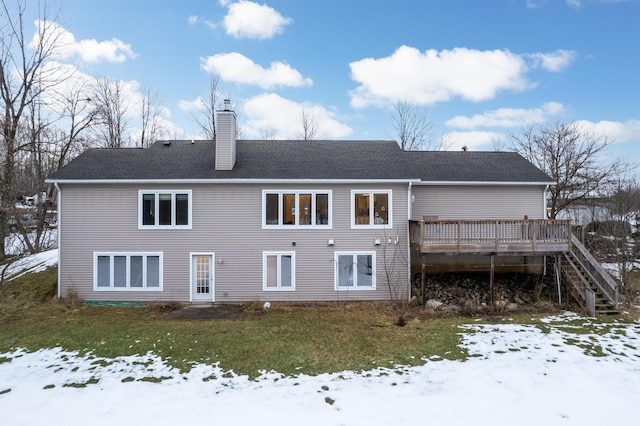 snow covered property with a chimney, stairway, roof with shingles, a deck, and a yard