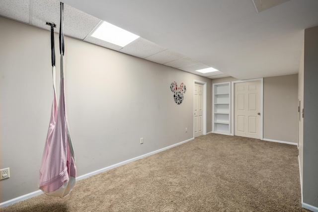 below grade area with a drop ceiling, carpet flooring, and baseboards