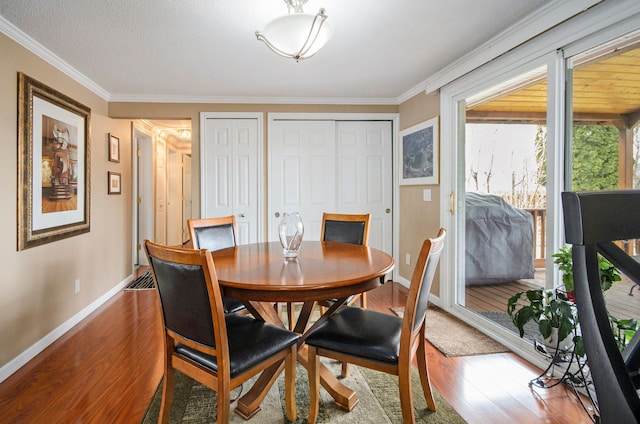 dining area with ornamental molding, a textured ceiling, baseboards, and wood finished floors