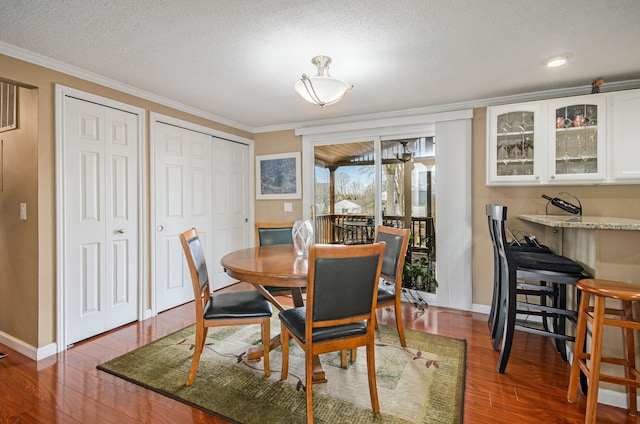 dining space with ornamental molding, a textured ceiling, baseboards, and wood finished floors