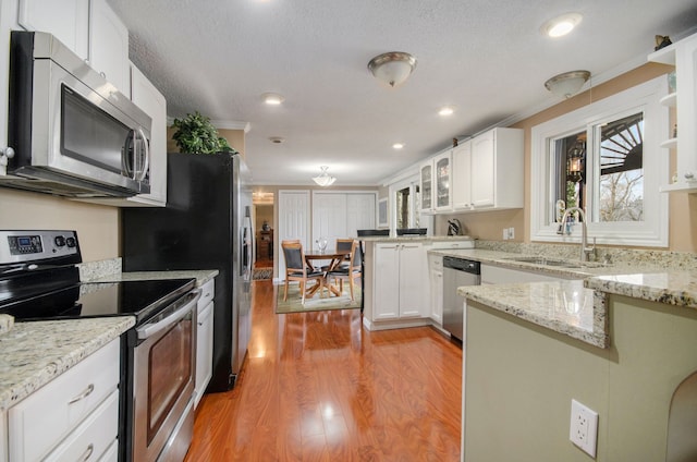 kitchen with light wood-style flooring, a sink, appliances with stainless steel finishes, a peninsula, and white cabinets