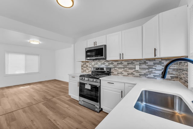 kitchen featuring white cabinets, decorative backsplash, stainless steel appliances, light countertops, and a sink