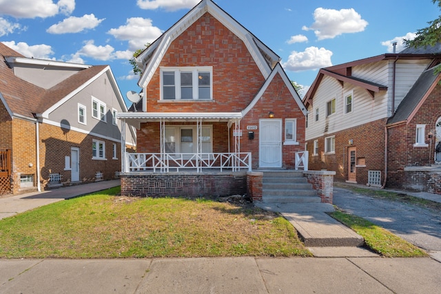 view of front of home featuring covered porch, brick siding, a front lawn, and a gambrel roof