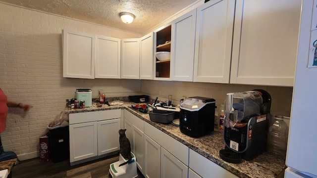 kitchen with dark wood finished floors, white cabinetry, a sink, a textured ceiling, and brick wall