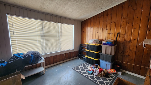 interior space with lofted ceiling, wood walls, concrete floors, and a textured ceiling