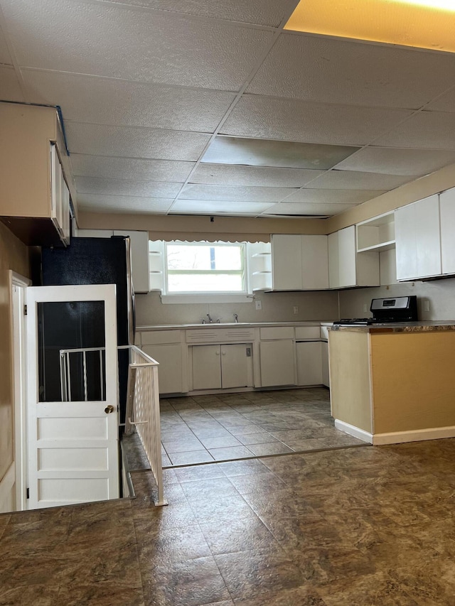 kitchen with a paneled ceiling, stainless steel range with gas cooktop, white cabinetry, and open shelves