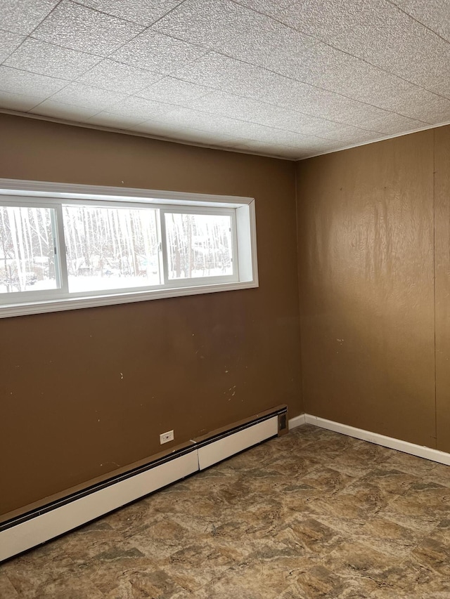 empty room with a baseboard heating unit, a wealth of natural light, and baseboards