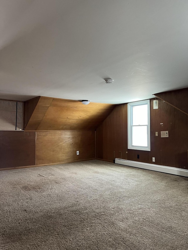 additional living space with a baseboard heating unit, vaulted ceiling, carpet flooring, and wooden walls