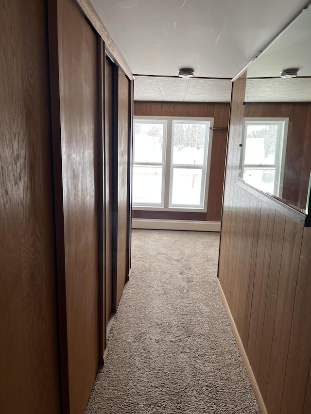 hallway featuring carpet flooring, wooden walls, and baseboards