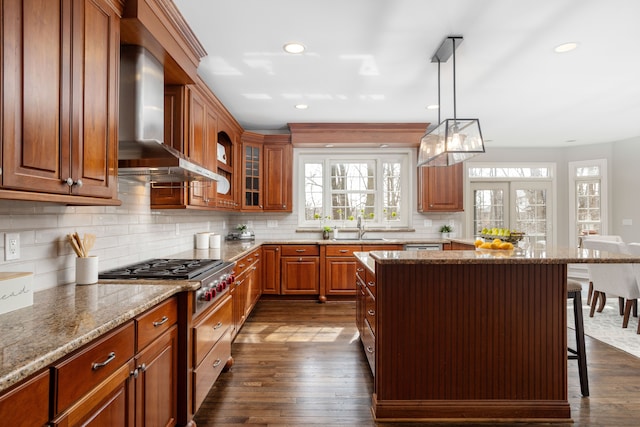 kitchen featuring dark wood-type flooring, wall chimney range hood, a breakfast bar area, and light stone countertops