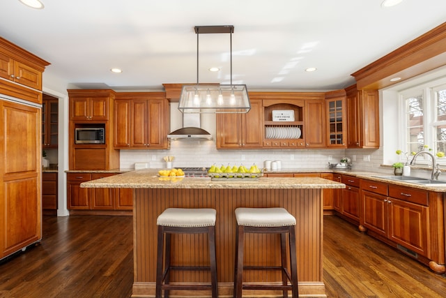 kitchen featuring stainless steel microwave, brown cabinets, dark wood-style flooring, and a sink