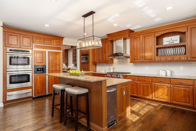 kitchen featuring a warming drawer, built in appliances, wall chimney range hood, brown cabinets, and a center island