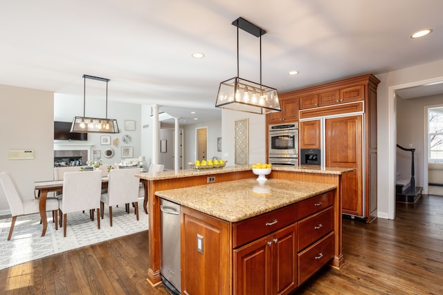 kitchen featuring stainless steel double oven, a kitchen island, a fireplace, dark wood-type flooring, and open floor plan