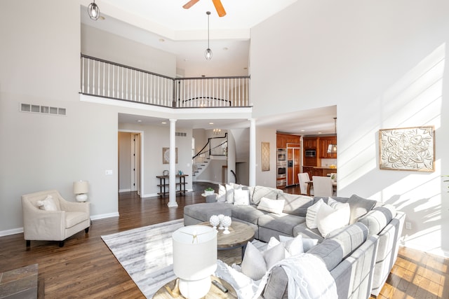 living area featuring visible vents, stairway, decorative columns, wood finished floors, and a ceiling fan