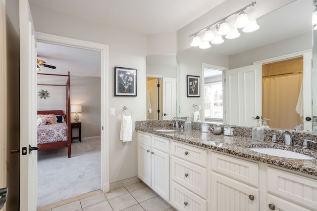 ensuite bathroom featuring tile patterned floors, double vanity, baseboards, and a sink