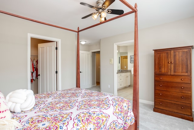 bedroom featuring light colored carpet, ensuite bathroom, baseboards, and ceiling fan