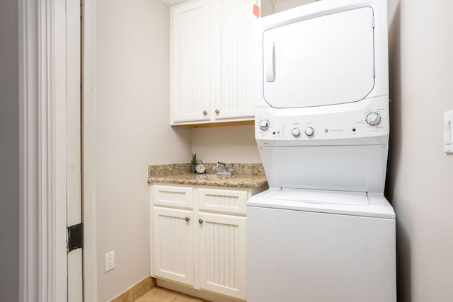 laundry area with light tile patterned floors, cabinet space, and stacked washer and clothes dryer