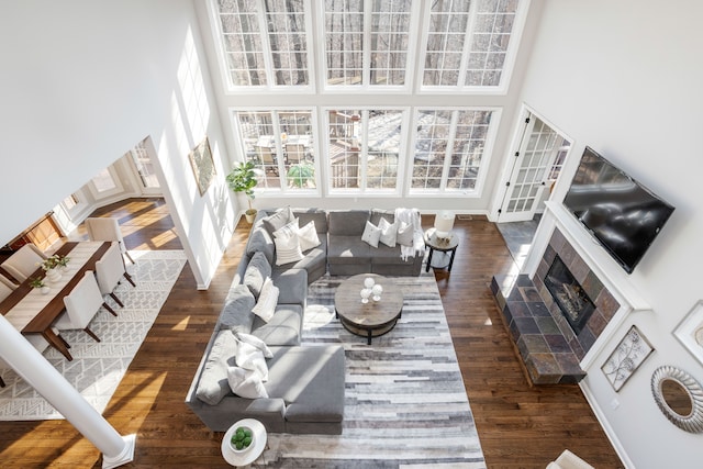 living room with a tiled fireplace, a high ceiling, wood finished floors, and baseboards