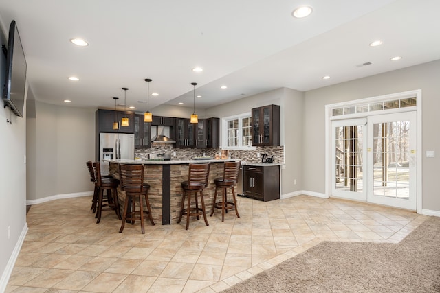 kitchen with visible vents, wall chimney range hood, a breakfast bar, decorative backsplash, and stainless steel fridge