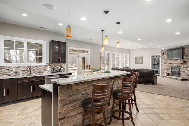 kitchen with a breakfast bar, dark brown cabinets, stainless steel dishwasher, tasteful backsplash, and a large fireplace