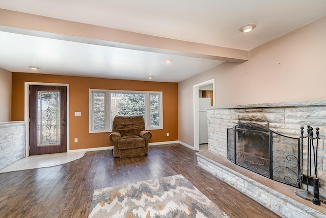 unfurnished living room featuring beam ceiling, a stone fireplace, baseboards, and wood finished floors