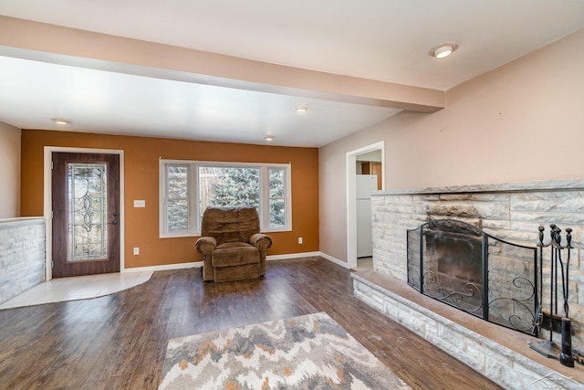 unfurnished living room with a stone fireplace, baseboards, wood finished floors, and beam ceiling