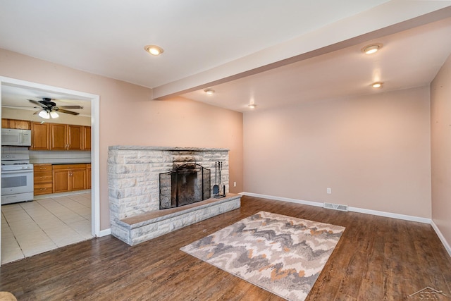 unfurnished living room featuring visible vents, baseboards, ceiling fan, a stone fireplace, and light wood-type flooring