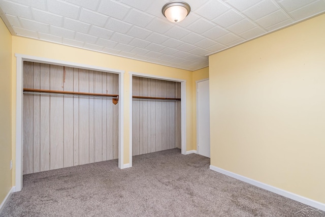 unfurnished bedroom with baseboards, two closets, and carpet floors