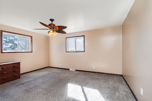 carpeted spare room with a ceiling fan, a healthy amount of sunlight, visible vents, and baseboards