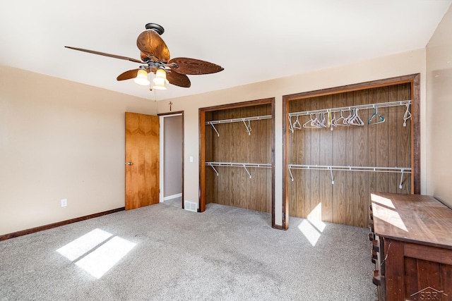 unfurnished bedroom featuring baseboards, carpet flooring, a ceiling fan, and two closets