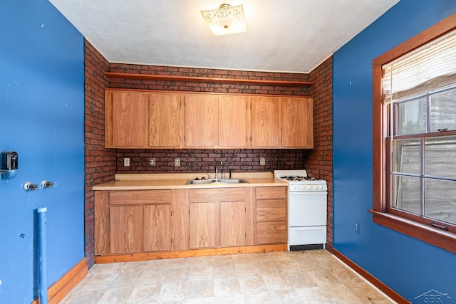 kitchen featuring brick wall, light countertops, a sink, and white gas stove