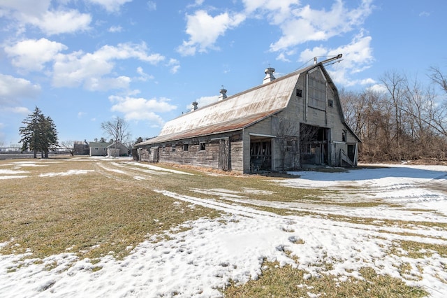 view of snow covered exterior featuring a gambrel roof, an outbuilding, and a barn