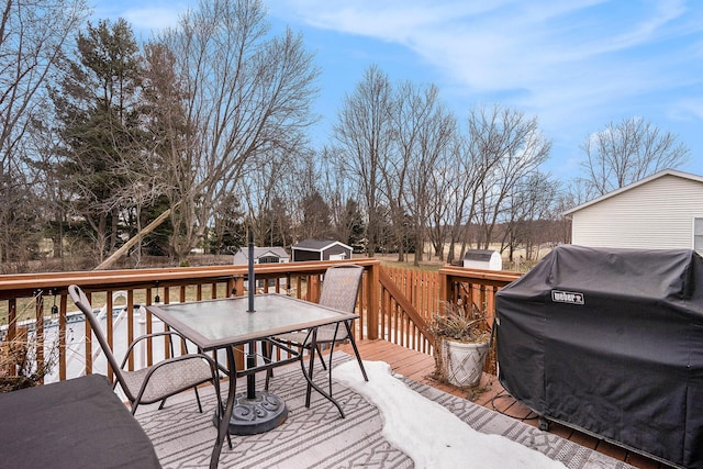 wooden deck featuring outdoor dining area, a shed, grilling area, and an outbuilding