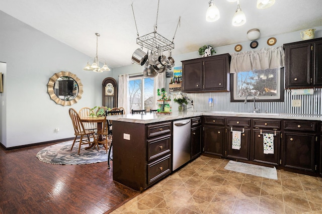 kitchen featuring light countertops, stainless steel dishwasher, a sink, vaulted ceiling, and a peninsula