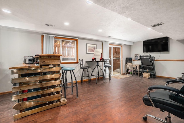 office space featuring a textured ceiling, wood finished floors, visible vents, and baseboards