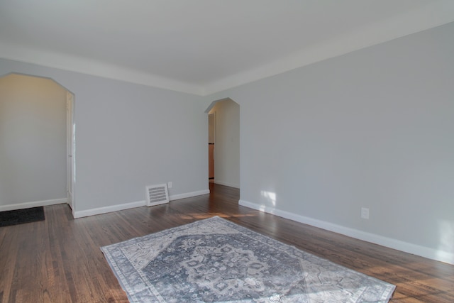 spare room with arched walkways, visible vents, baseboards, and wood finished floors