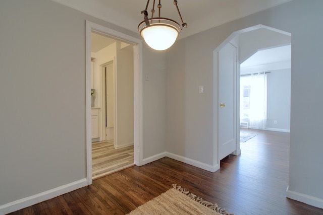 hallway featuring arched walkways, wood finished floors, and baseboards